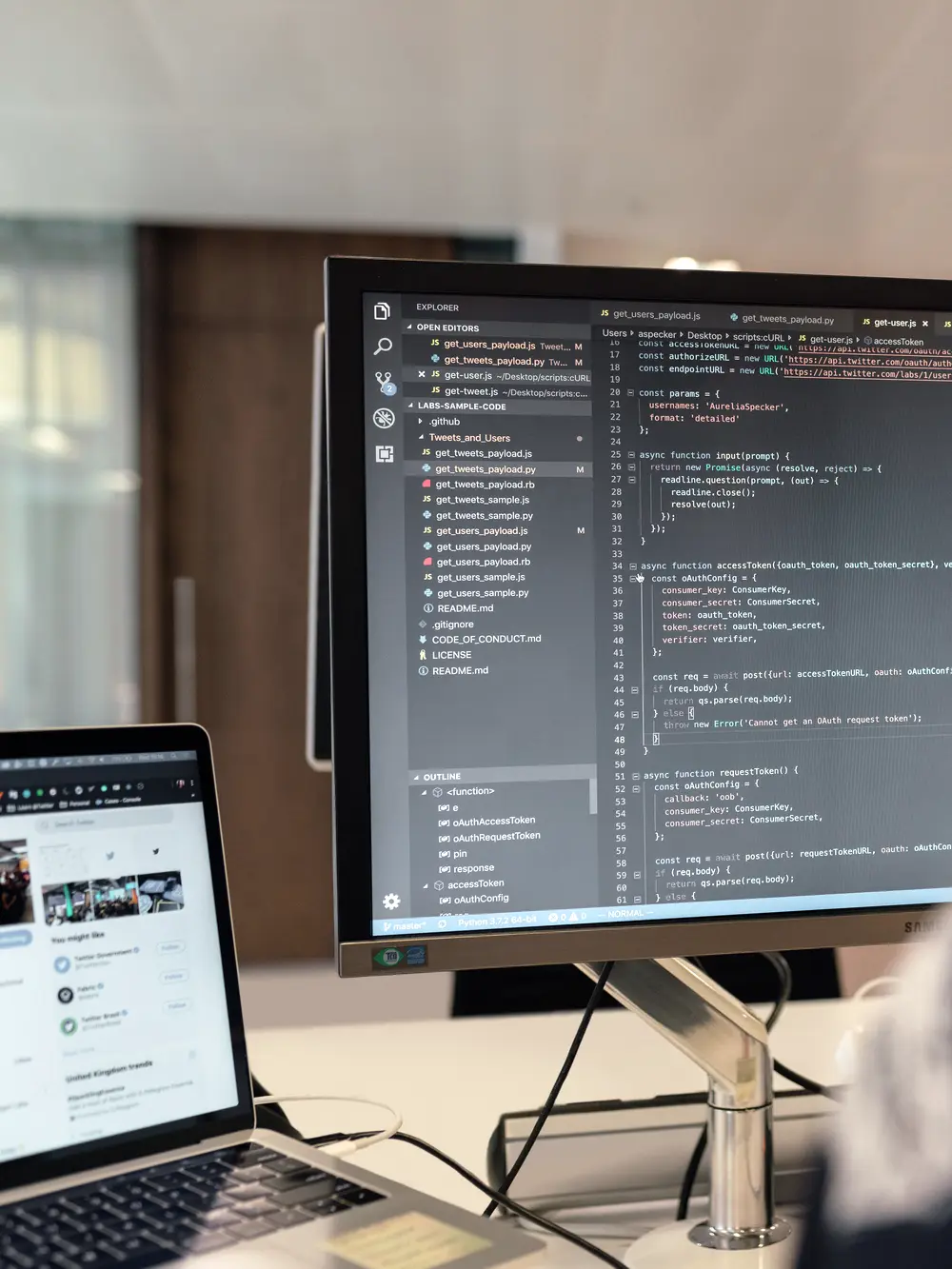 A code editor open on a desk monitor beside a laptop