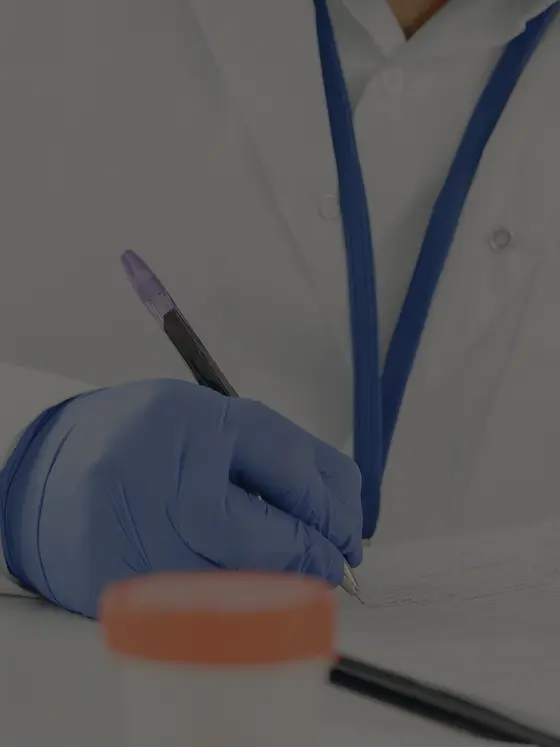 A gloved hand writing notes onto a printed page at a lab bench